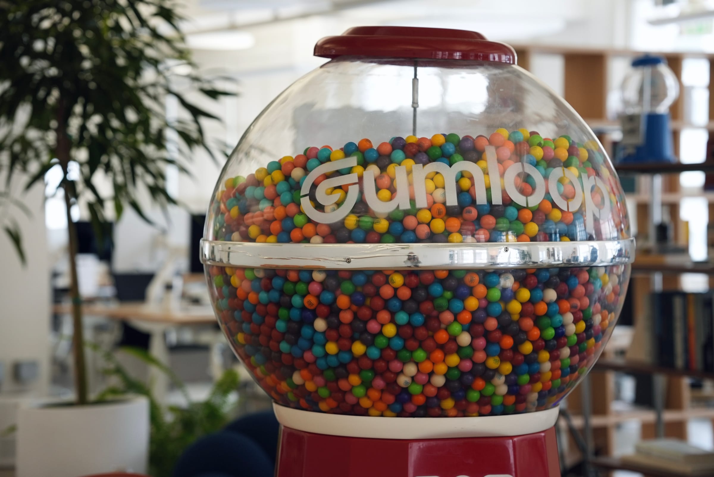 The Gumloop-branded gumball machine standing on the office floor, packed with coloured gumballs